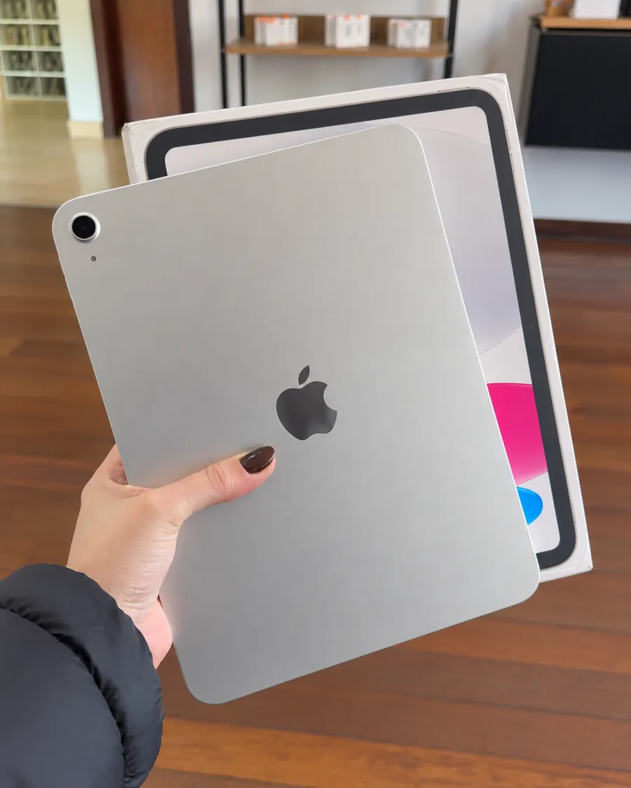 Mão segurando um iPad prateado com a caixa ao fundo