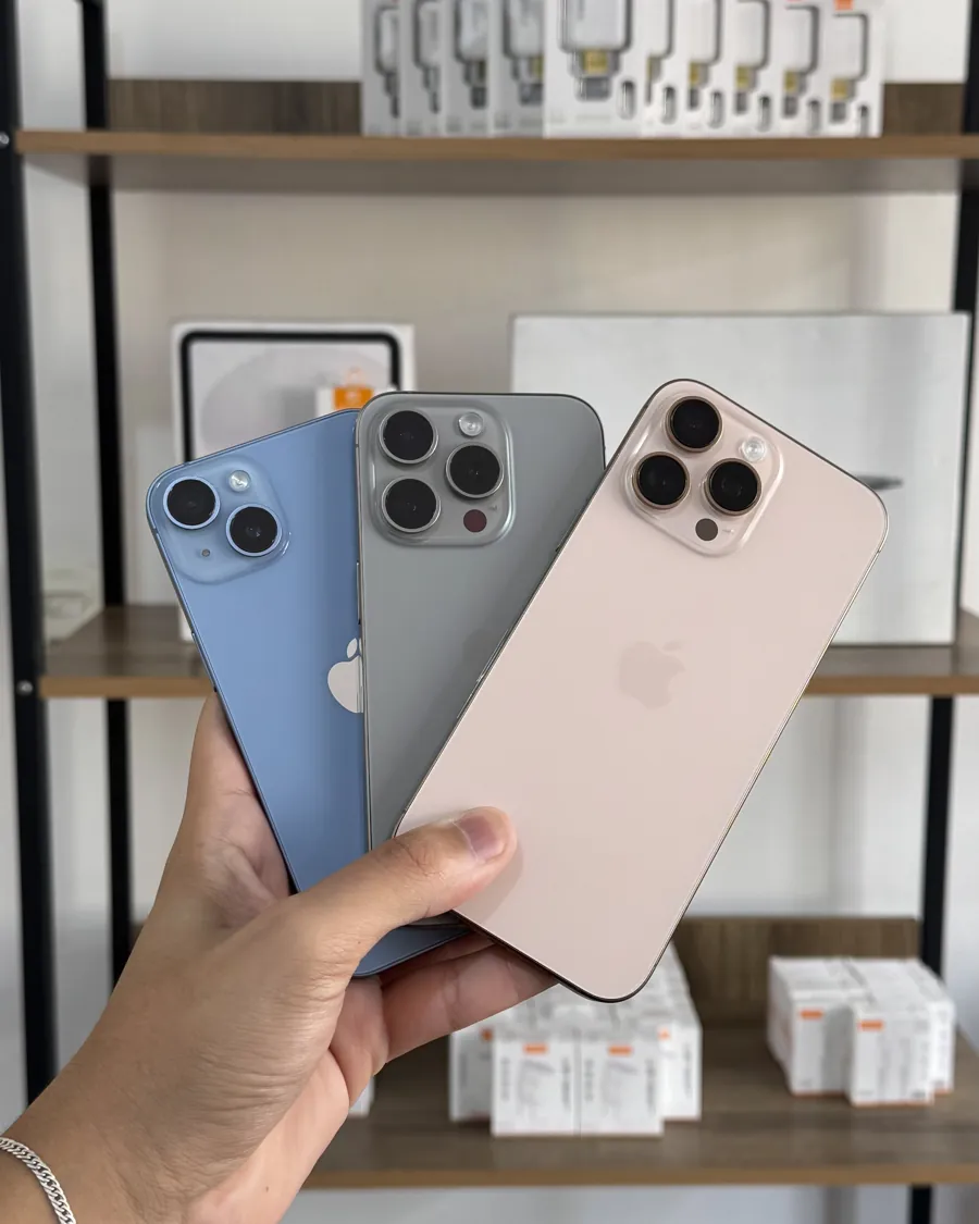Mão segurando três iPhones em frente à estante da loja